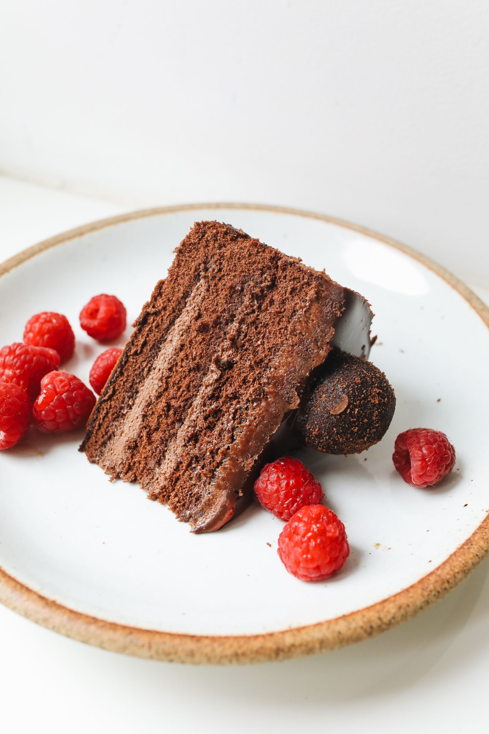 Close-up of a chocolate cake slice on a ceramic plate, garnished with fresh raspberries