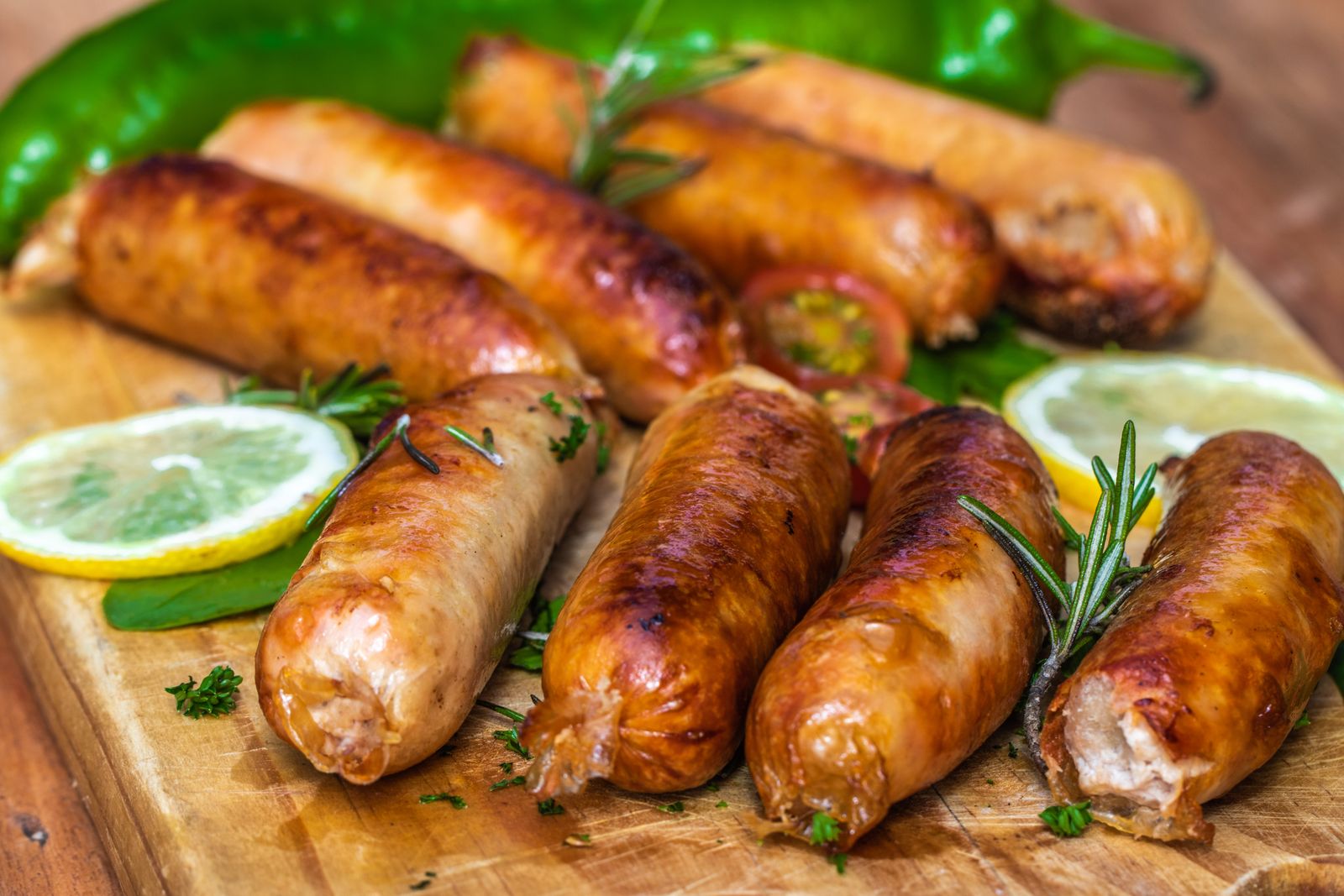 Juicy grilled sausages on a wooden board with lemon slices and herbs