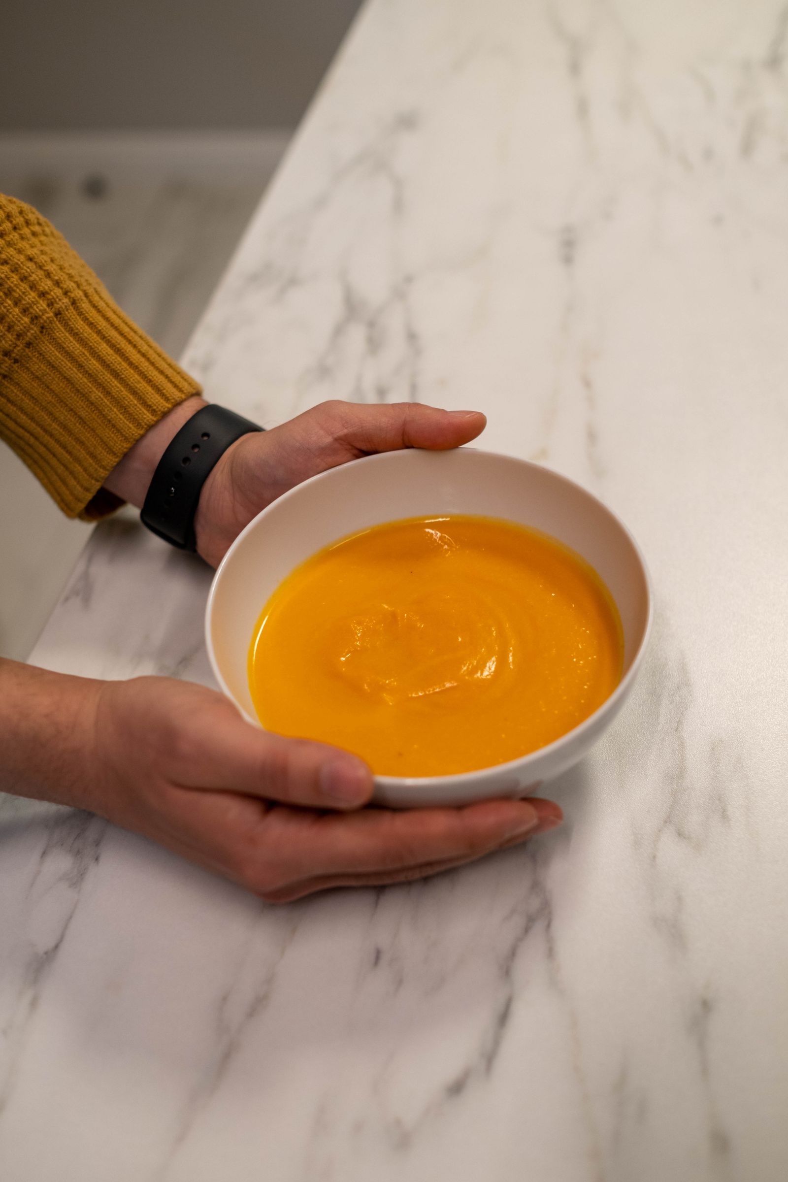 Warm pumpkin soup served in a ceramic bowl held by hands over a marble surface