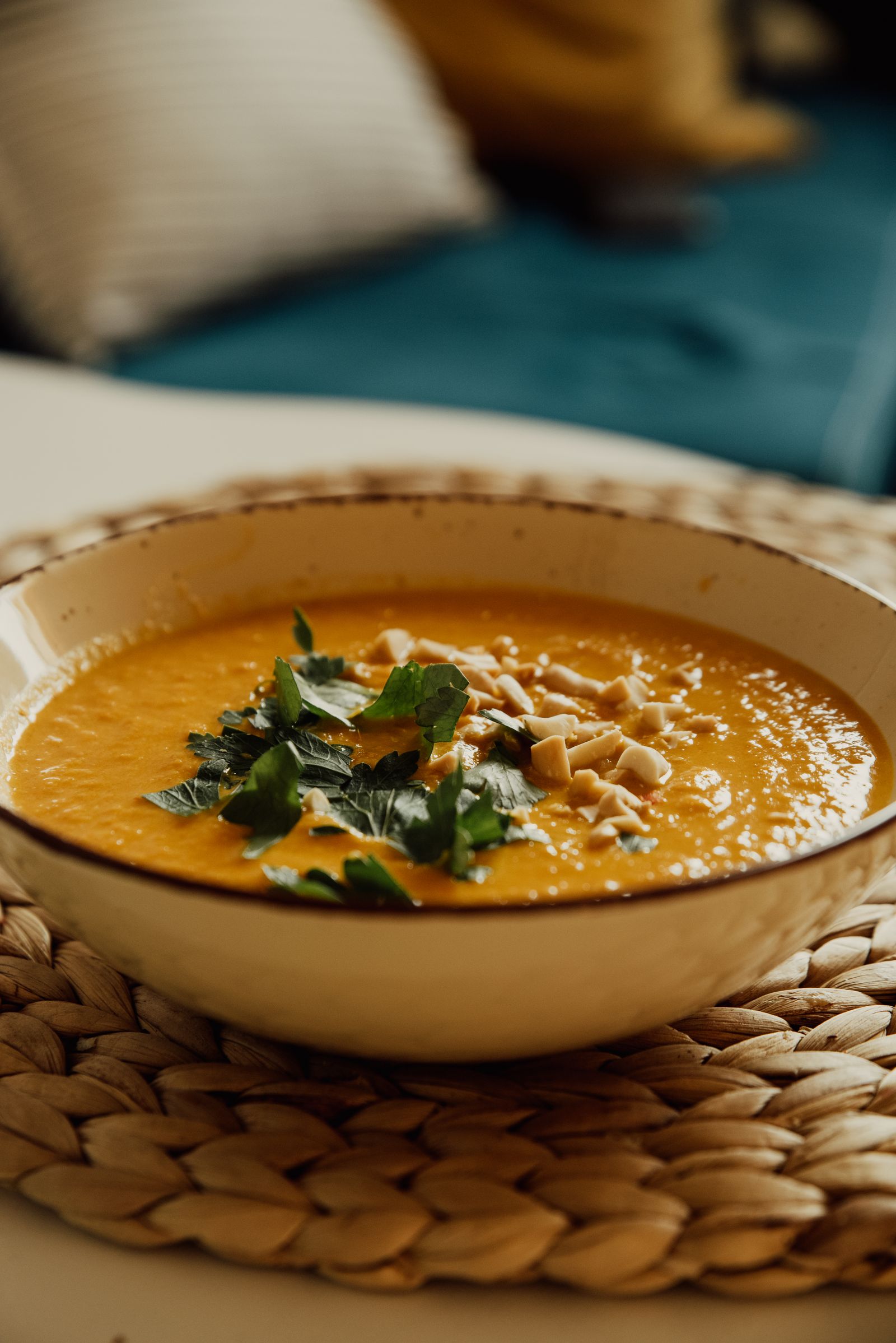 A warm bowl of pumpkin soup garnished with herbs and nuts on a woven mat
