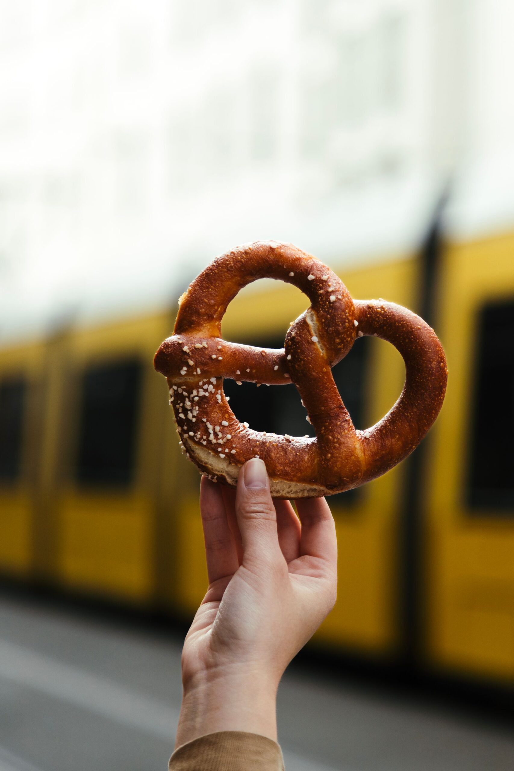 Person holding a pretzel in front of a yellow tram