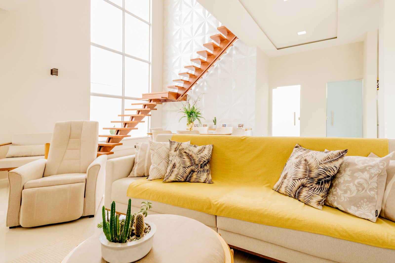A brightly lit modern living room with a yellow sofa, stairs, and elegant decor