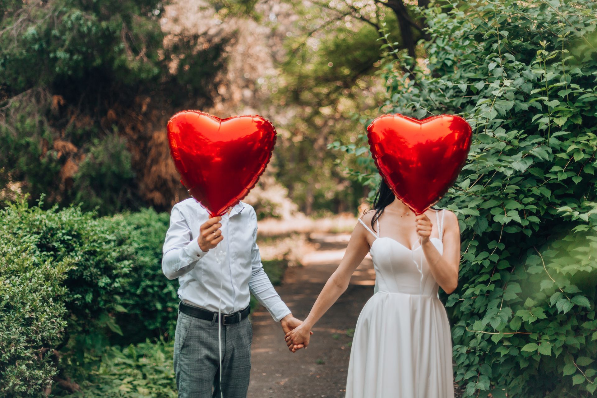 Couple holding red heart-shaped balloons outdoors