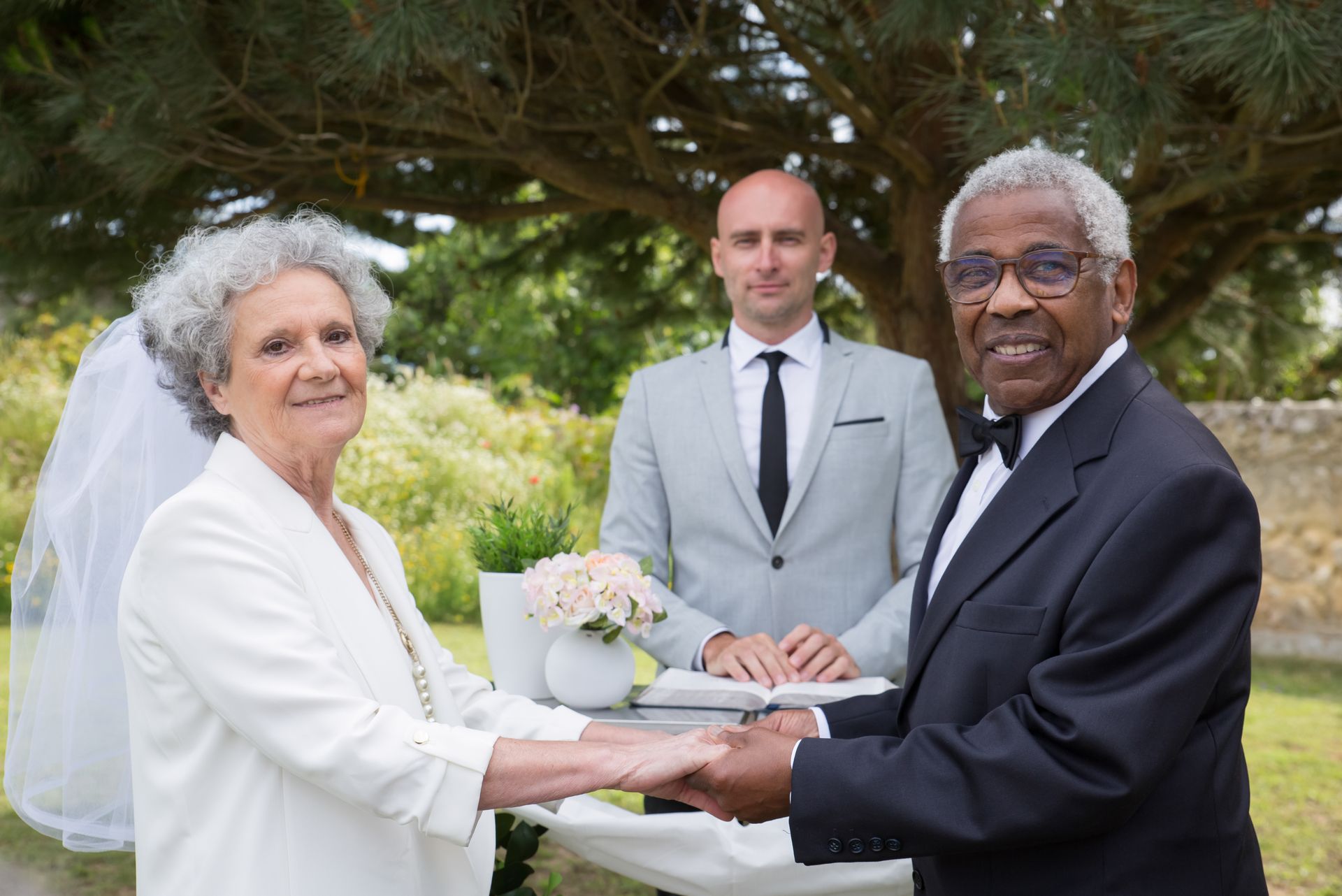 Elderly couple holding hands during an outdoor wedding ceremony