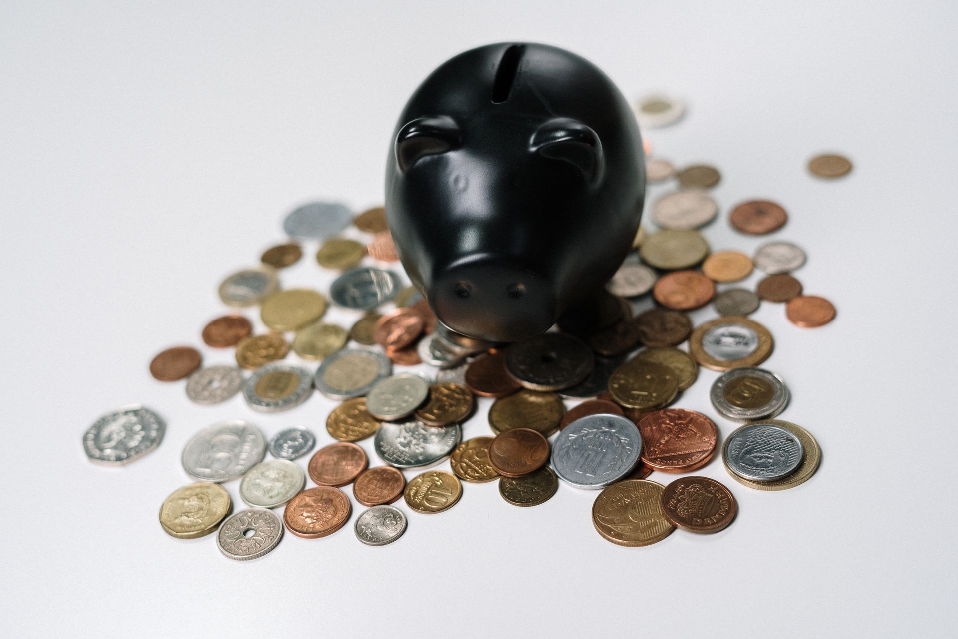 Black piggy bank surrounded by coins on a white surface