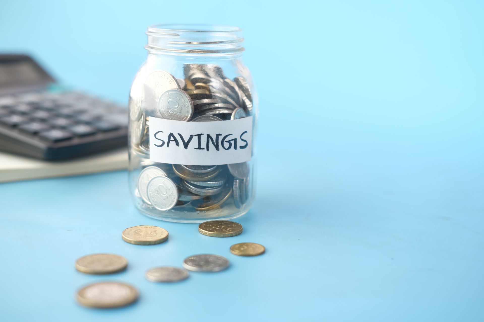 Glass jar labeled Savings filled with coins beside a calculator