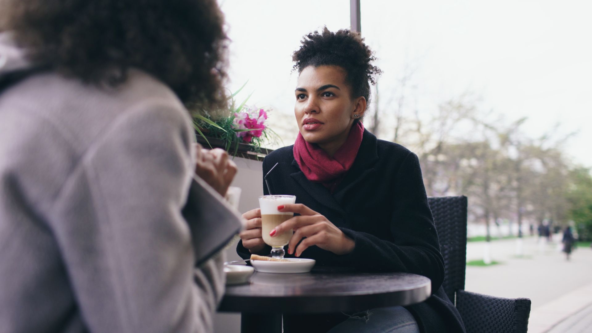 Two women having a conversation over coffee at an outdoor cafe on a bright day