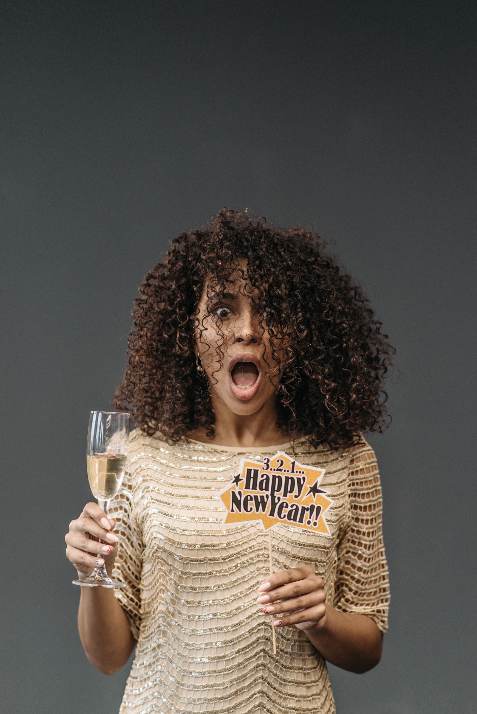 Woman in a festive dress holding champagne and a Happy New Year sign