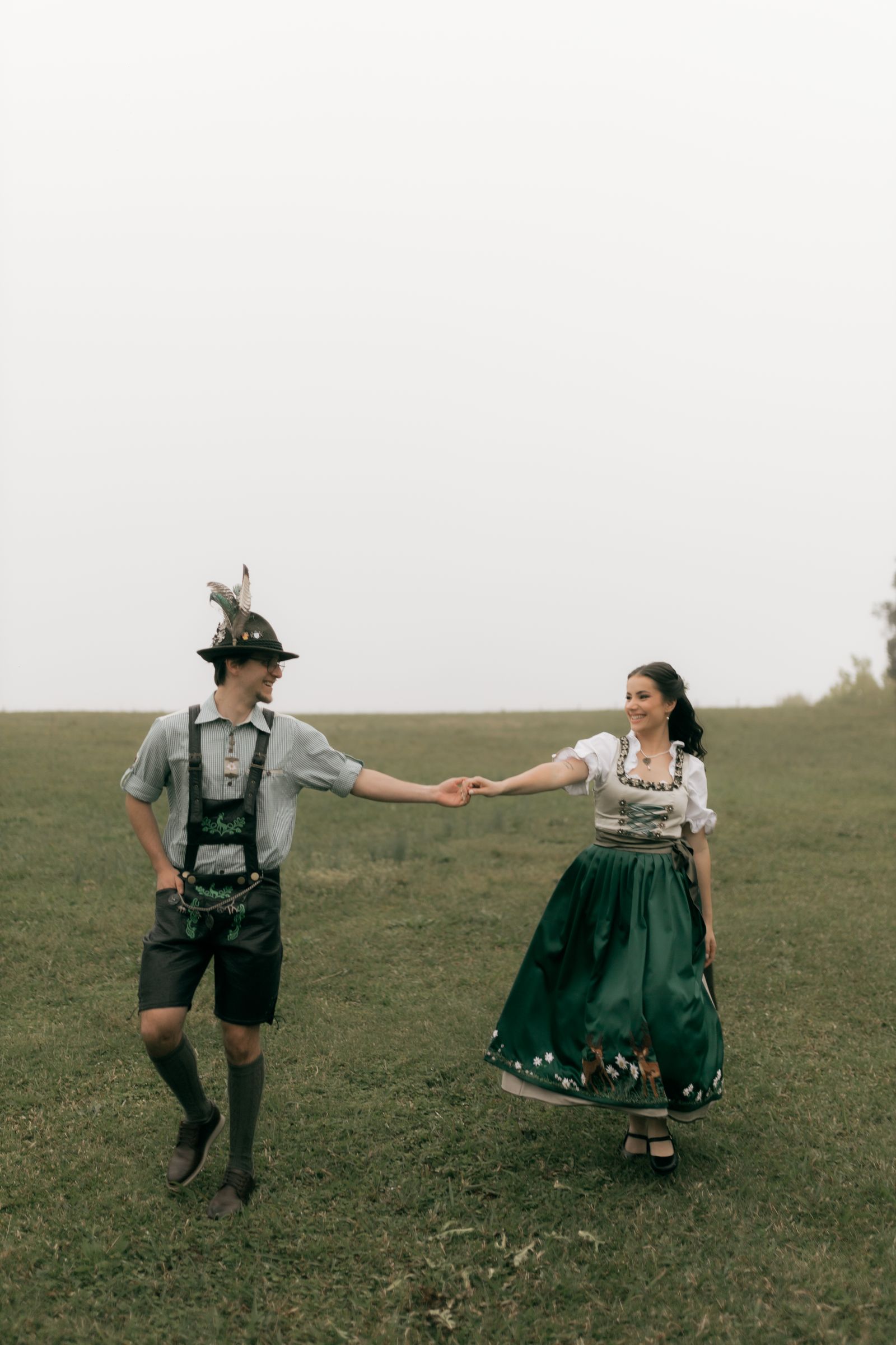 Couple in traditional Bavarian Tracht, dirndl and lederhosen, dancing in a field