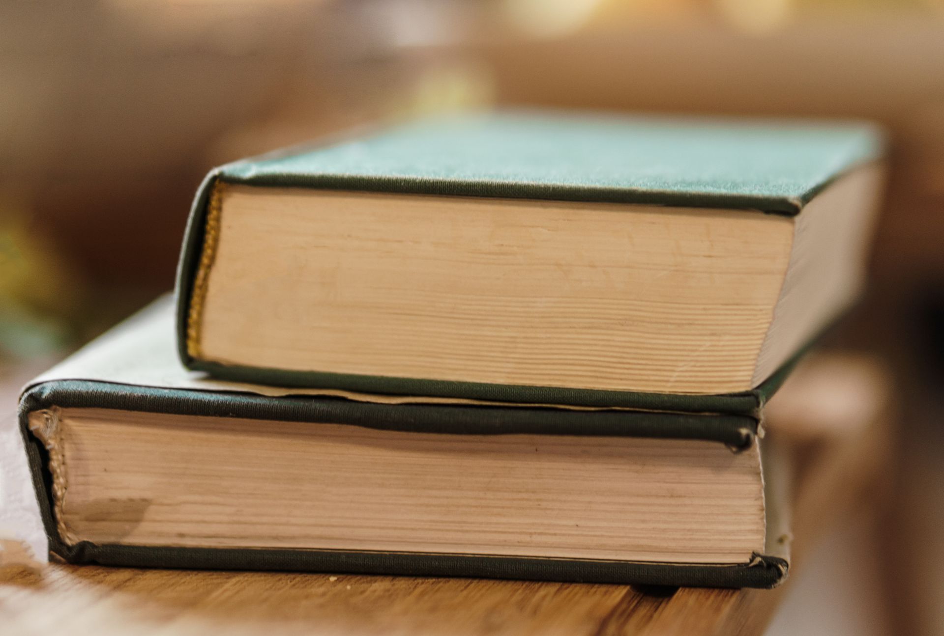 Old hardcover textbooks stacked on a wooden table in sunlight