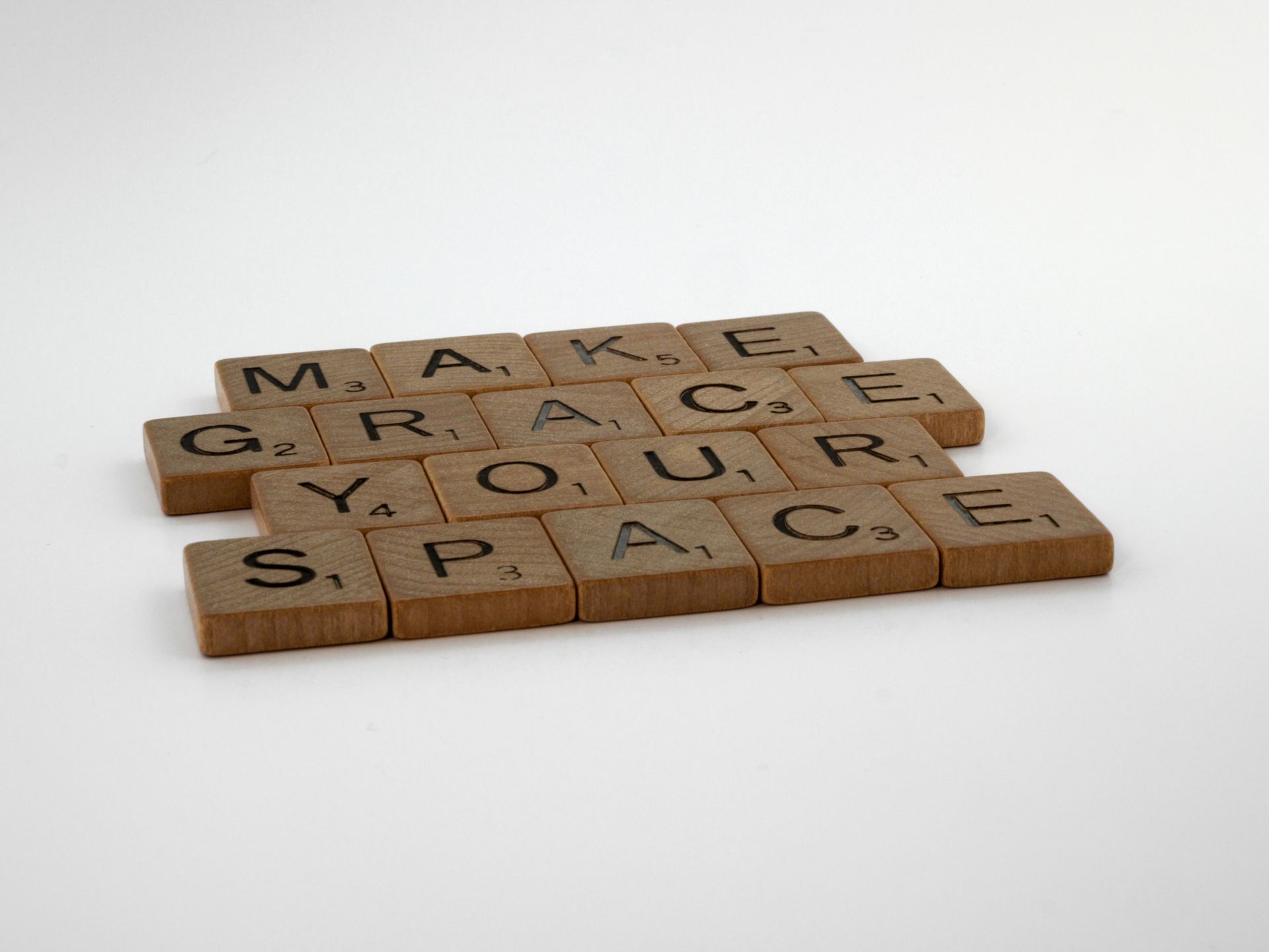 Wooden Scrabble tiles form the message "Make Grace Your Space" on a white surface.