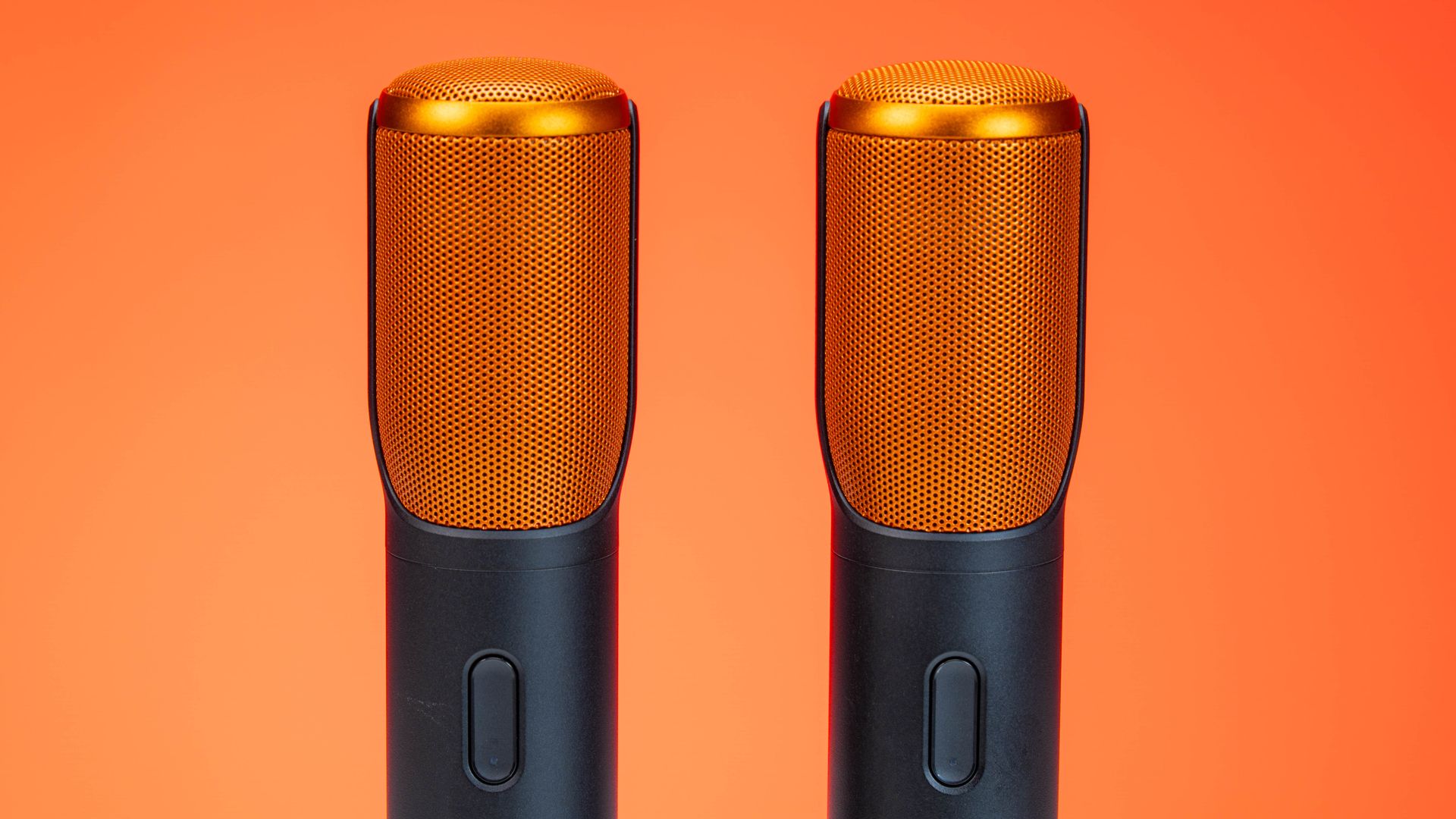 Vibrant photo of two modern microphones against an orange background, highlighting technology.