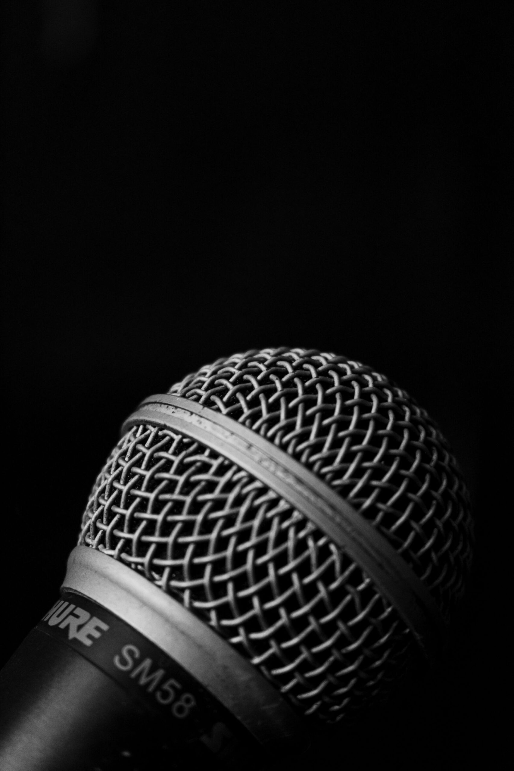 Detailed close-up of a Shure SM58 microphone on a black background, emphasizing texture and details.