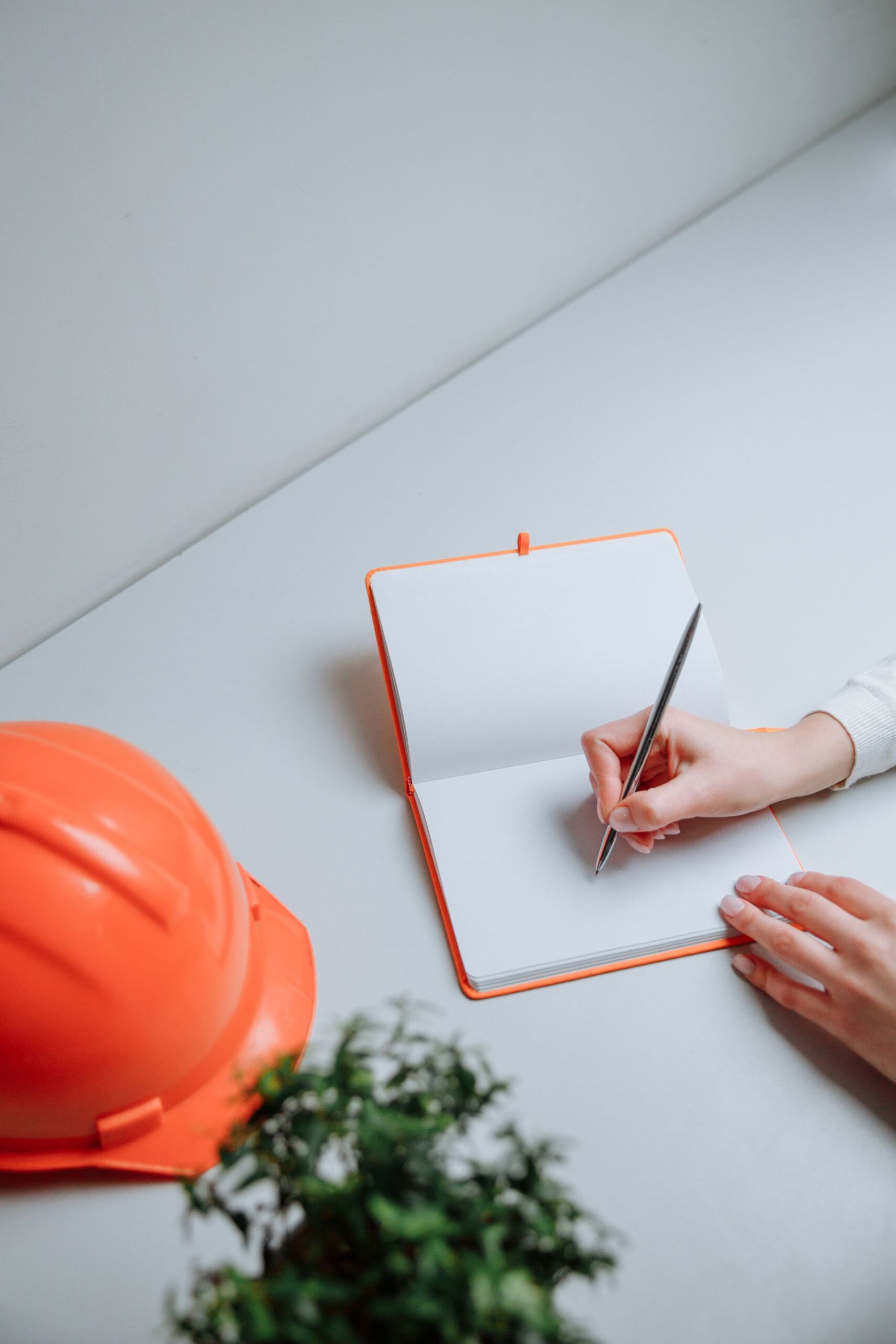 A person writing notes in a notebook beside a hardhat
