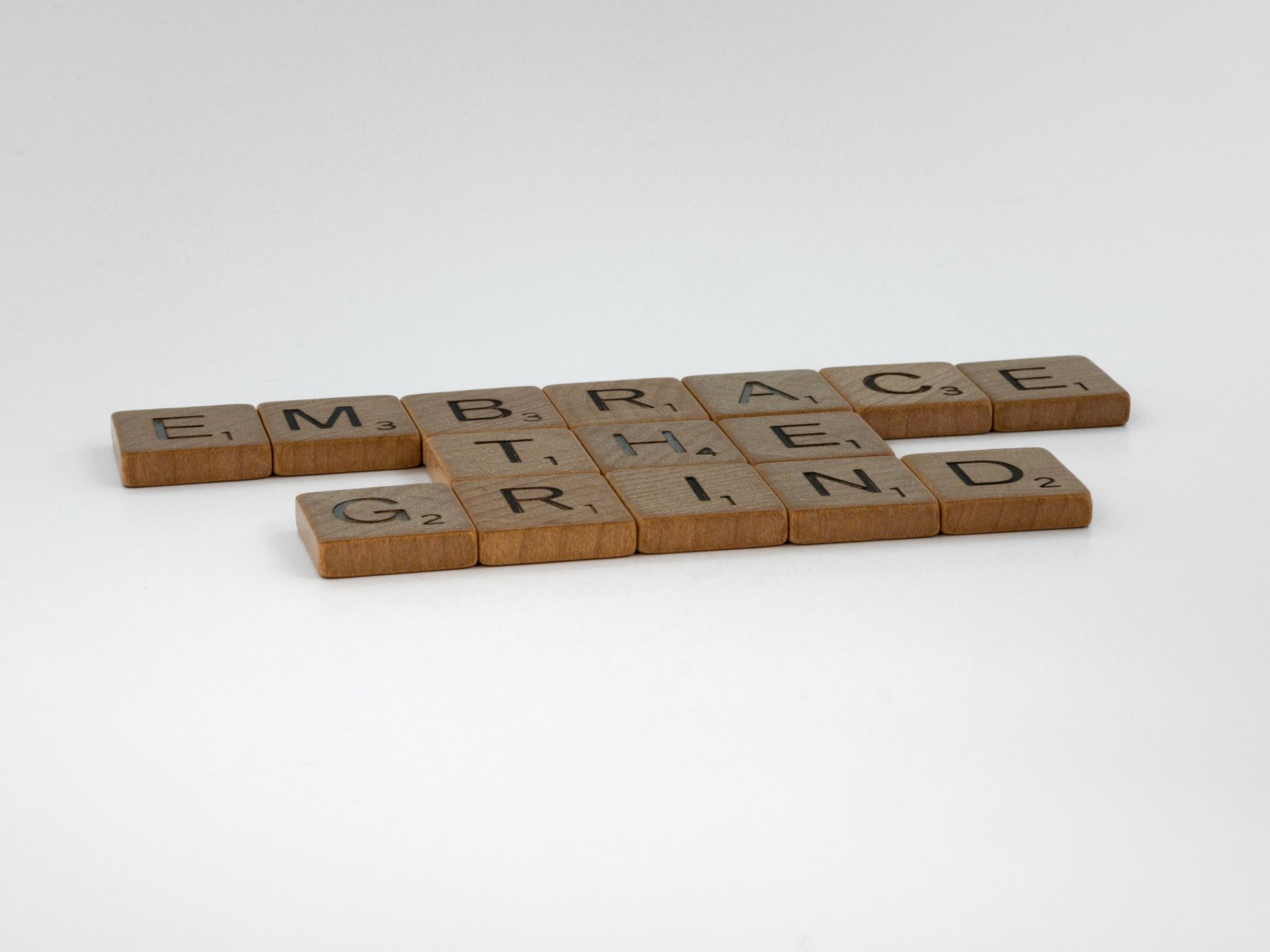 Scrabble tiles spelling Embrace the Grind on white