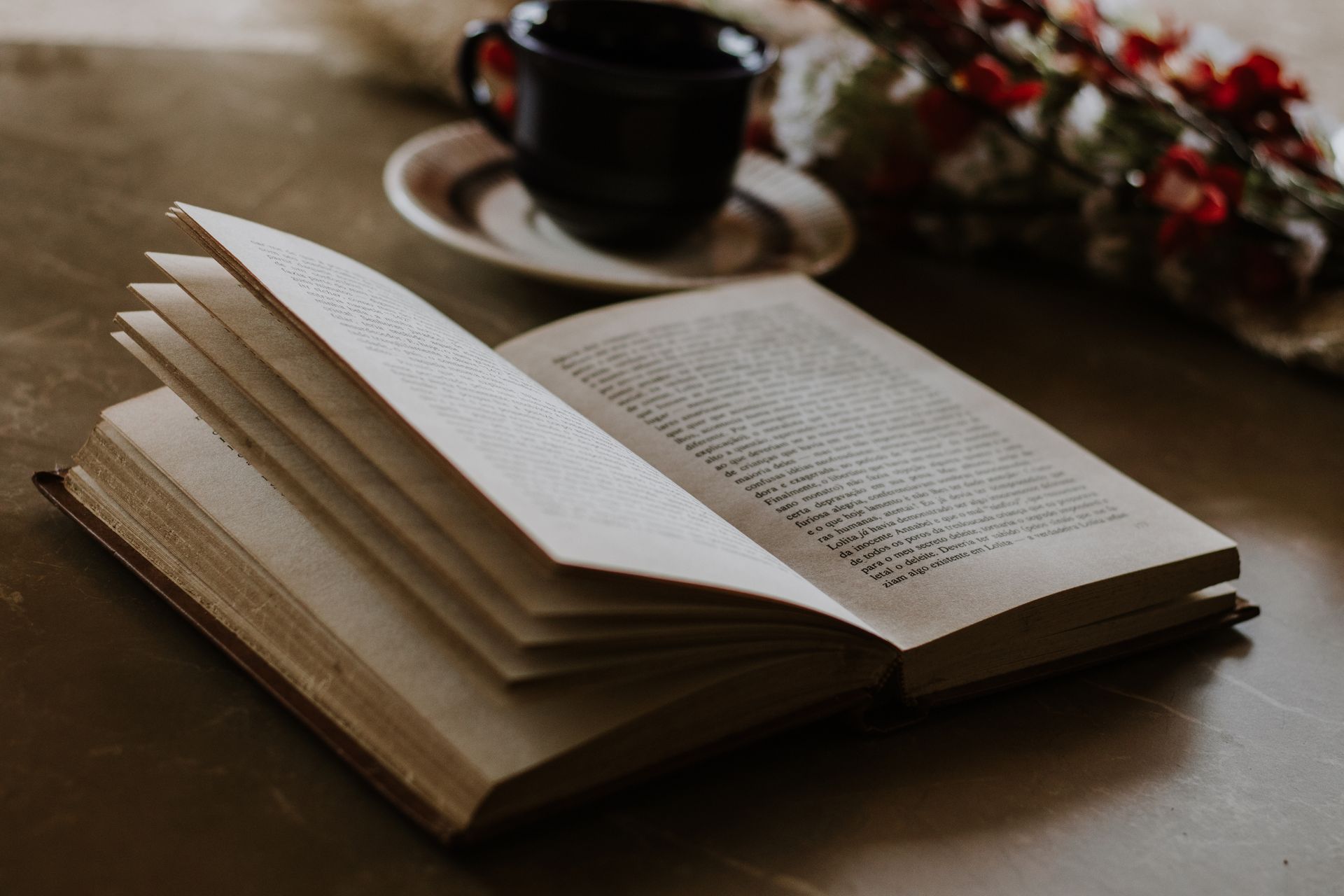 Open book by flowers and a cup on a wooden table