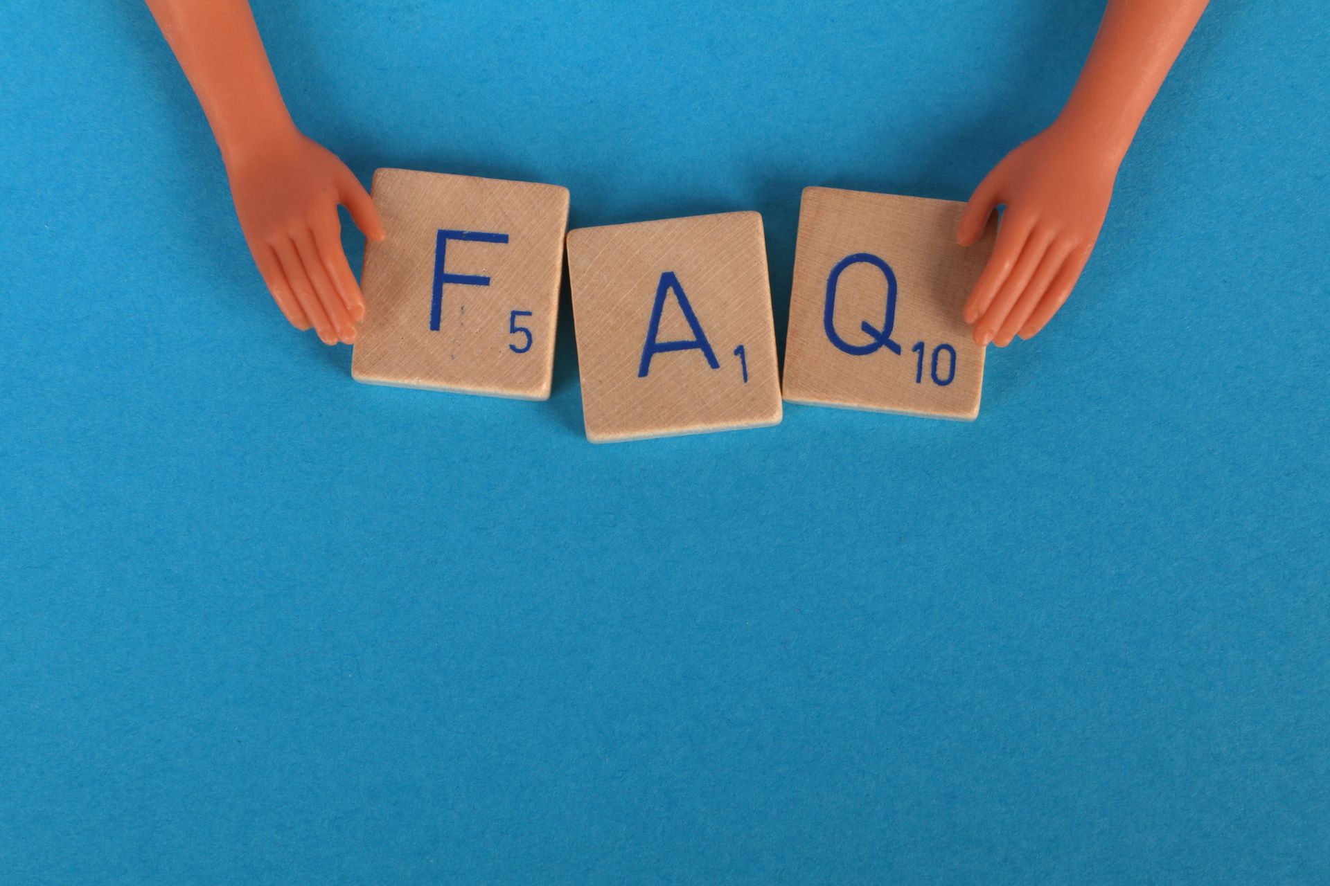 Scrabble tiles spelling FAQ on a blue surface