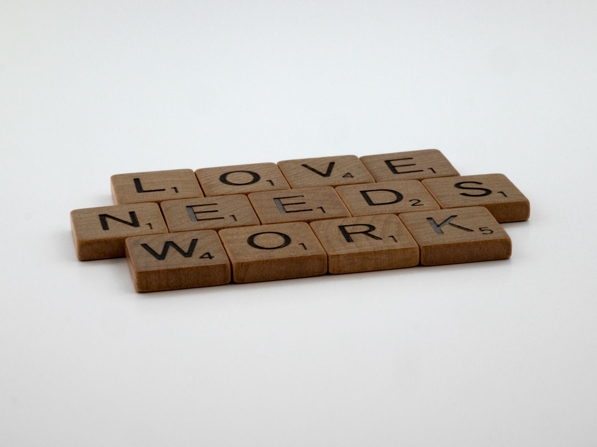 Scrabble tiles spelling Love Needs Work on white