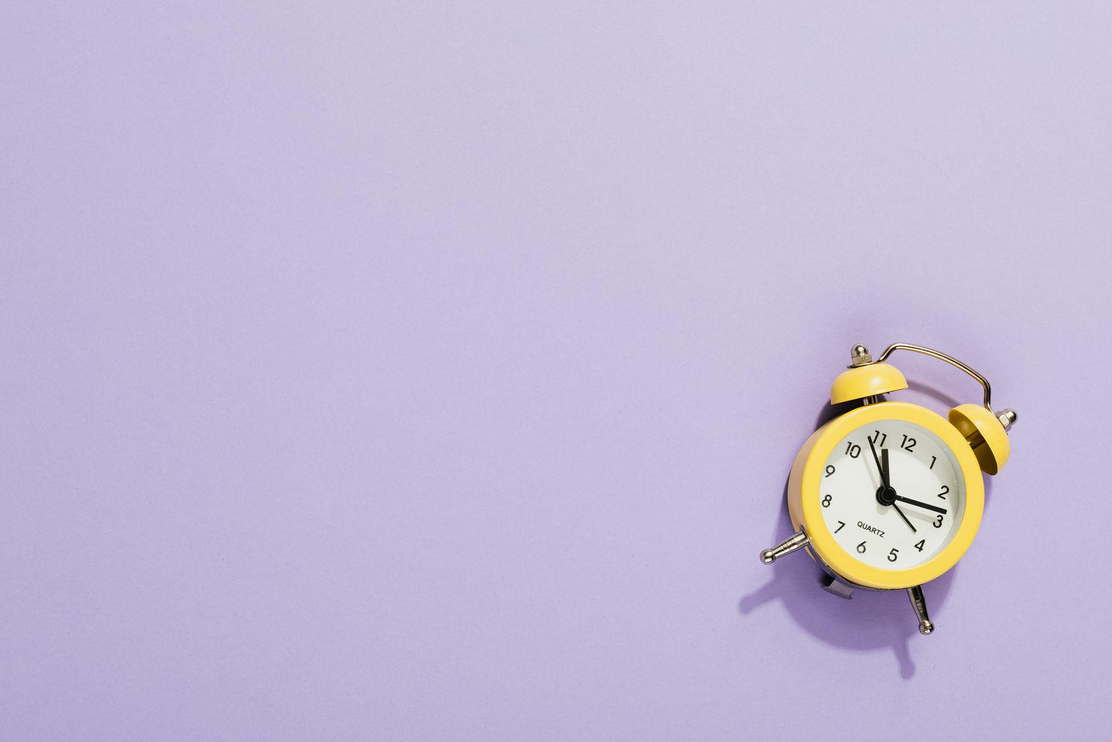 A vibrant yellow alarm clock on a purple surface