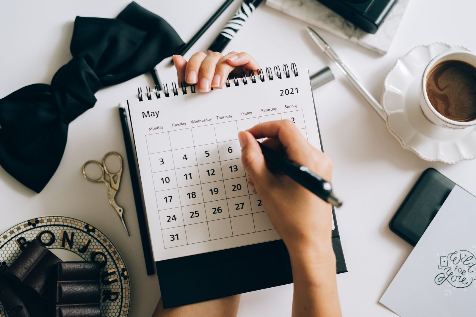 Top view of hands using a planner with coffee and accessories, focused on calendar