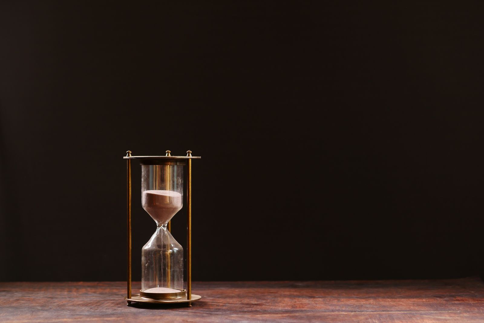 A classic hourglass with sand trickling down, symbolizing the passage of time, against a dark background