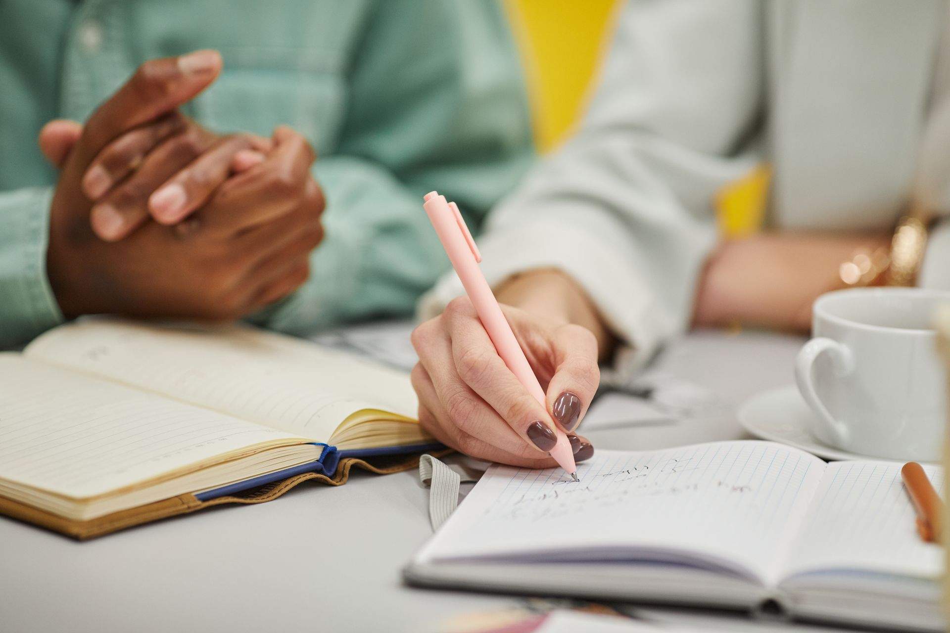 Close-up of diverse hands writing in notebooks with a pen during a meeting.