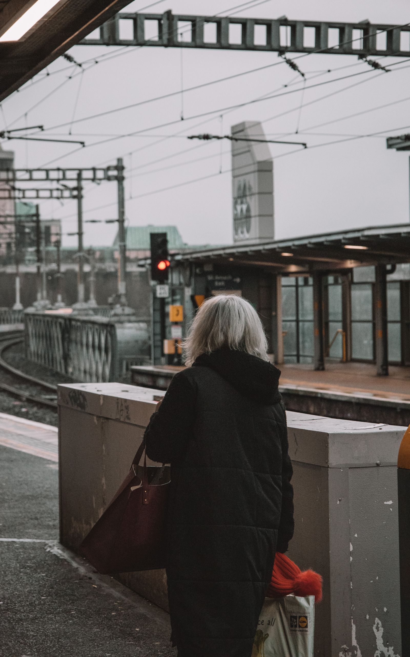 Back view of a woman waiting at a train station platform on a cloudy day