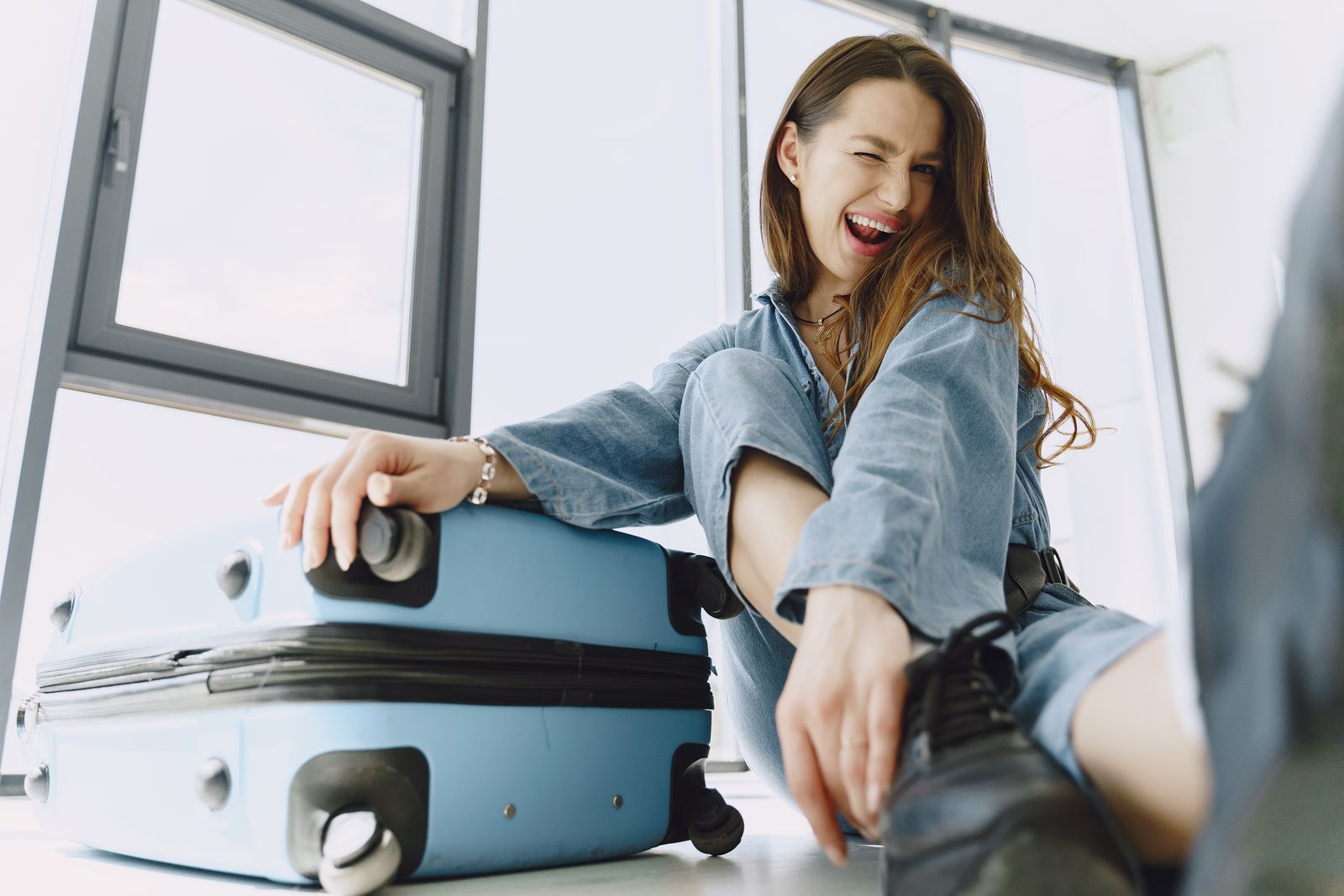 Cheerful young woman with suitcase in airport, ready for her adventure