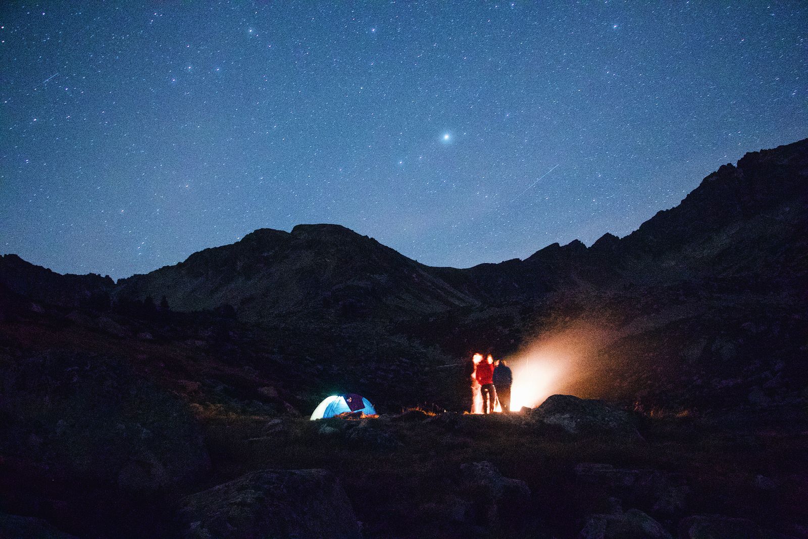 Camping under a starry sky with a glowing campfire and mountains