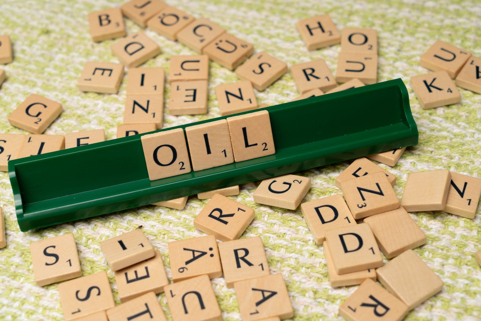 Wooden Scrabble tiles spelling Oil on a green knitted surface