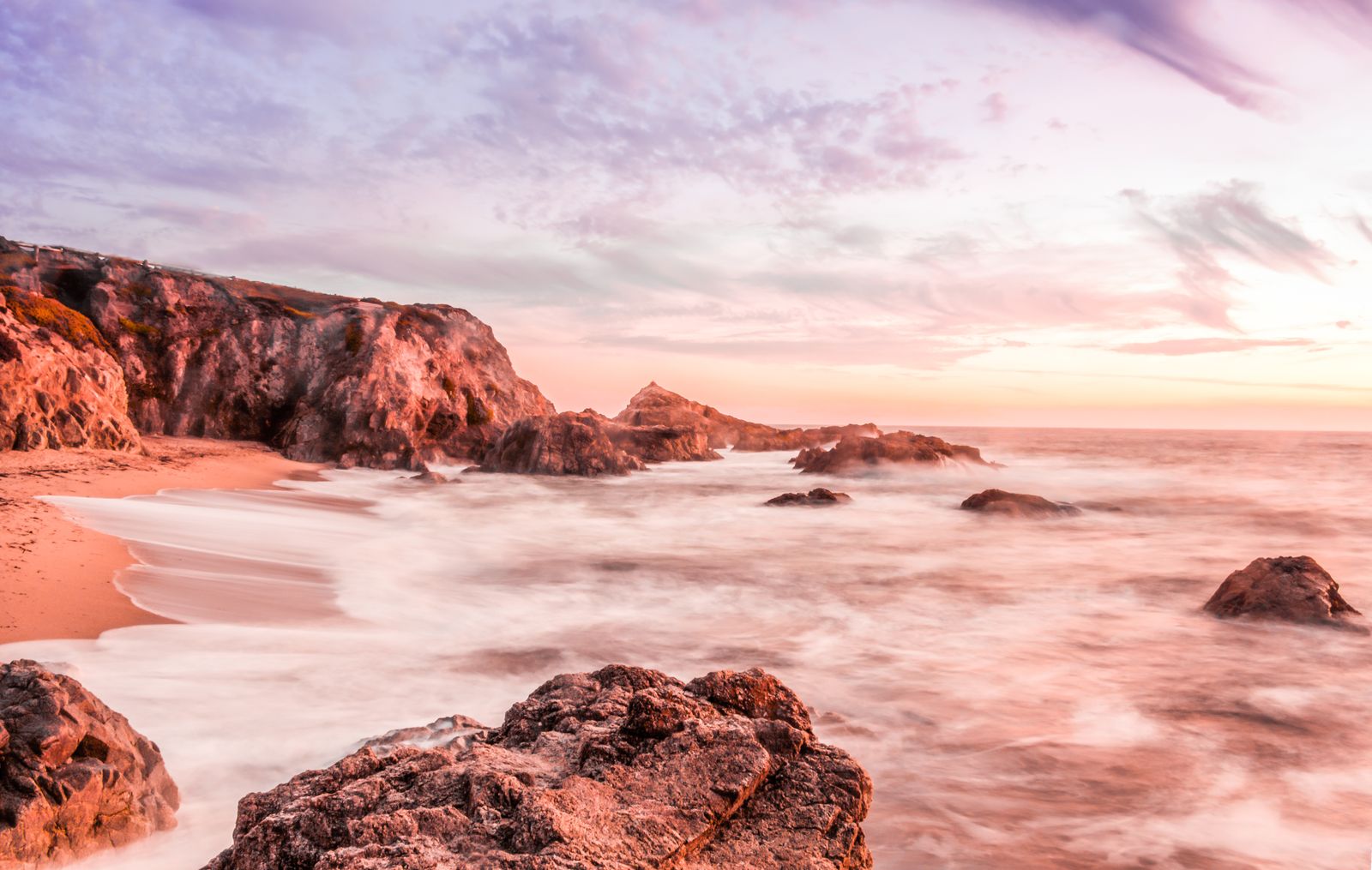 Vibrant pink and orange sunrise over rocky seashore with gentle waves