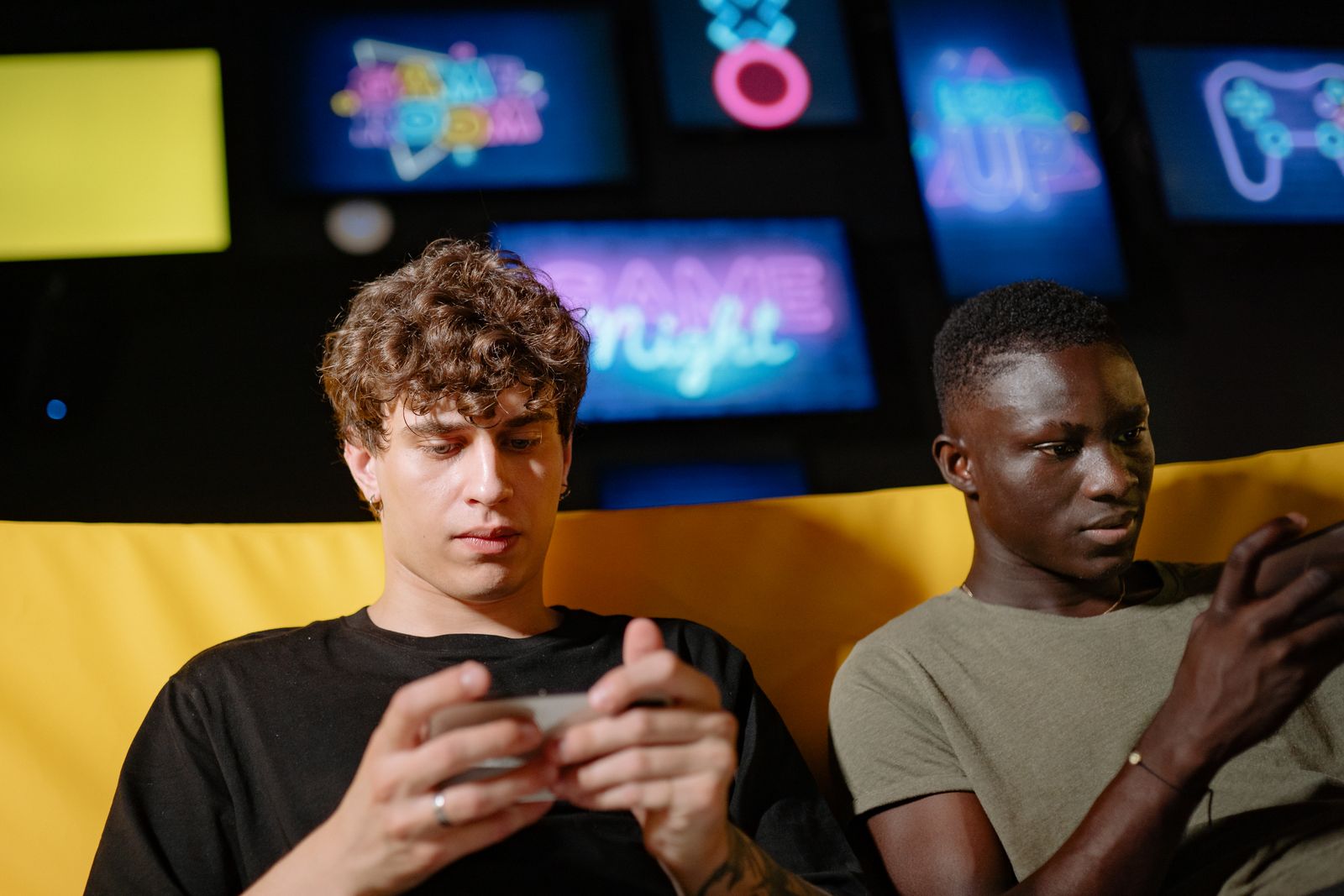 Two friends playing mobile games indoors on their smartphones