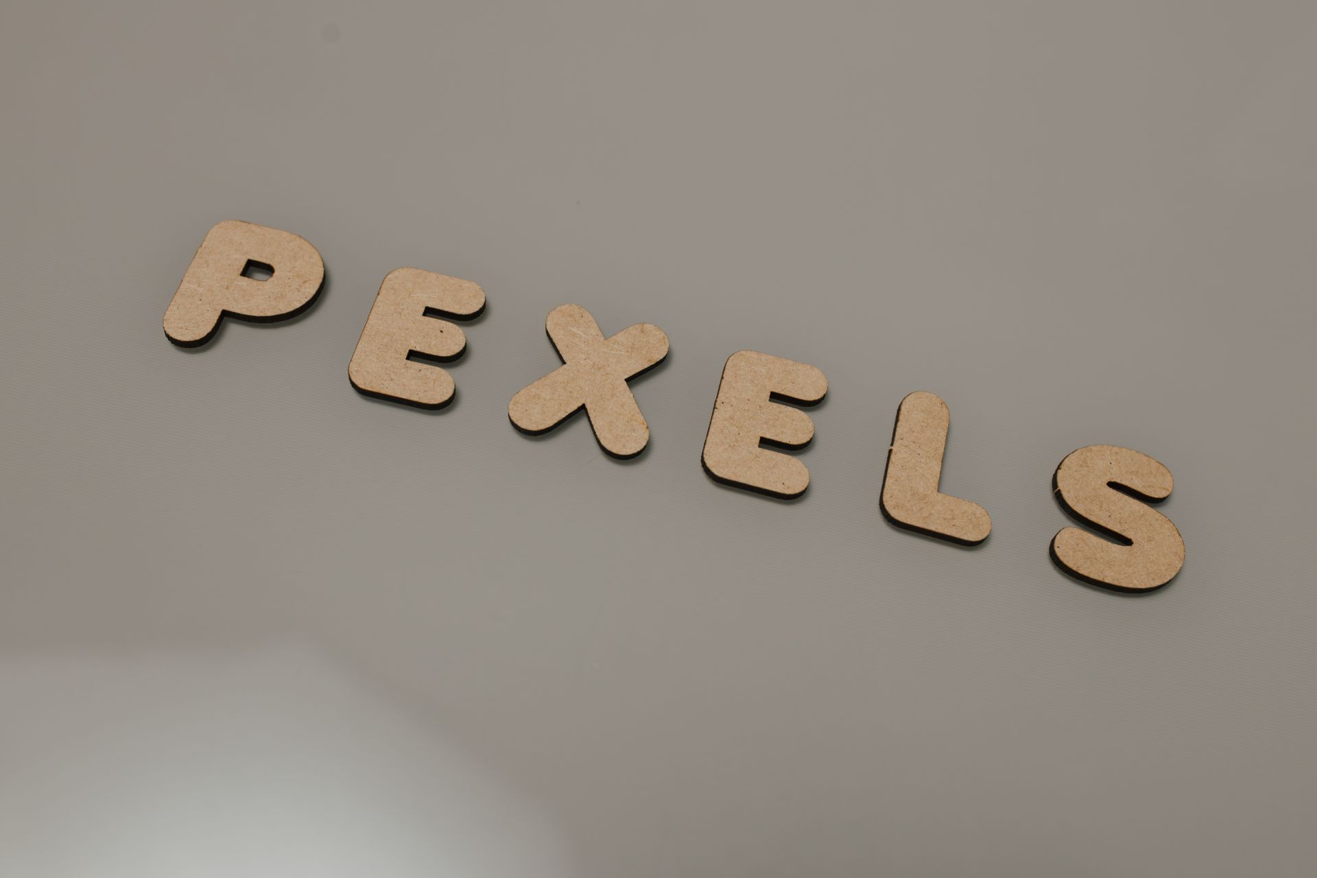 Wooden cutout letters spelling 'PEXELS' on a neutral surface, offering space for text.