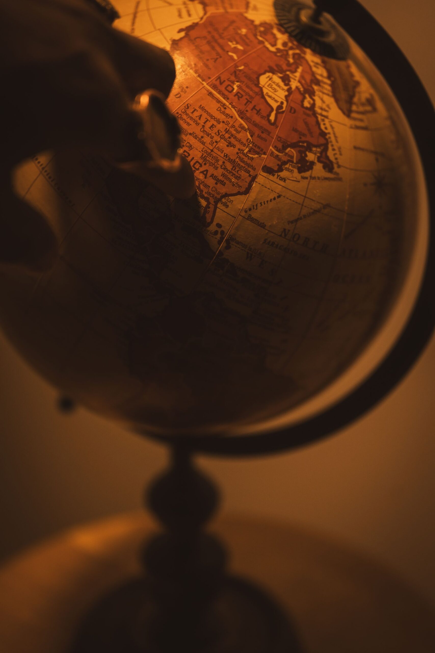 A vintage globe in warm tones with a hand pointing to a location.