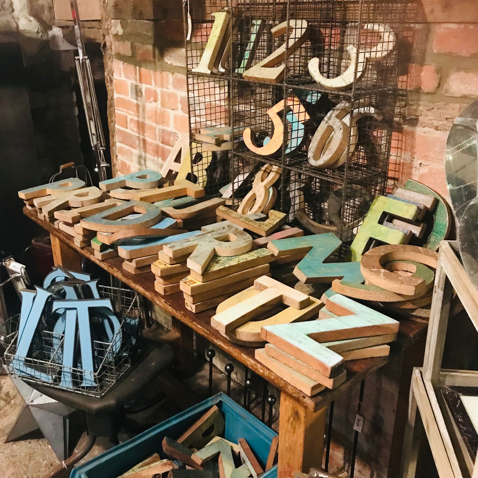 Assorted vintage wooden letters and numbers on a rustic table and wire rack in a workshop.