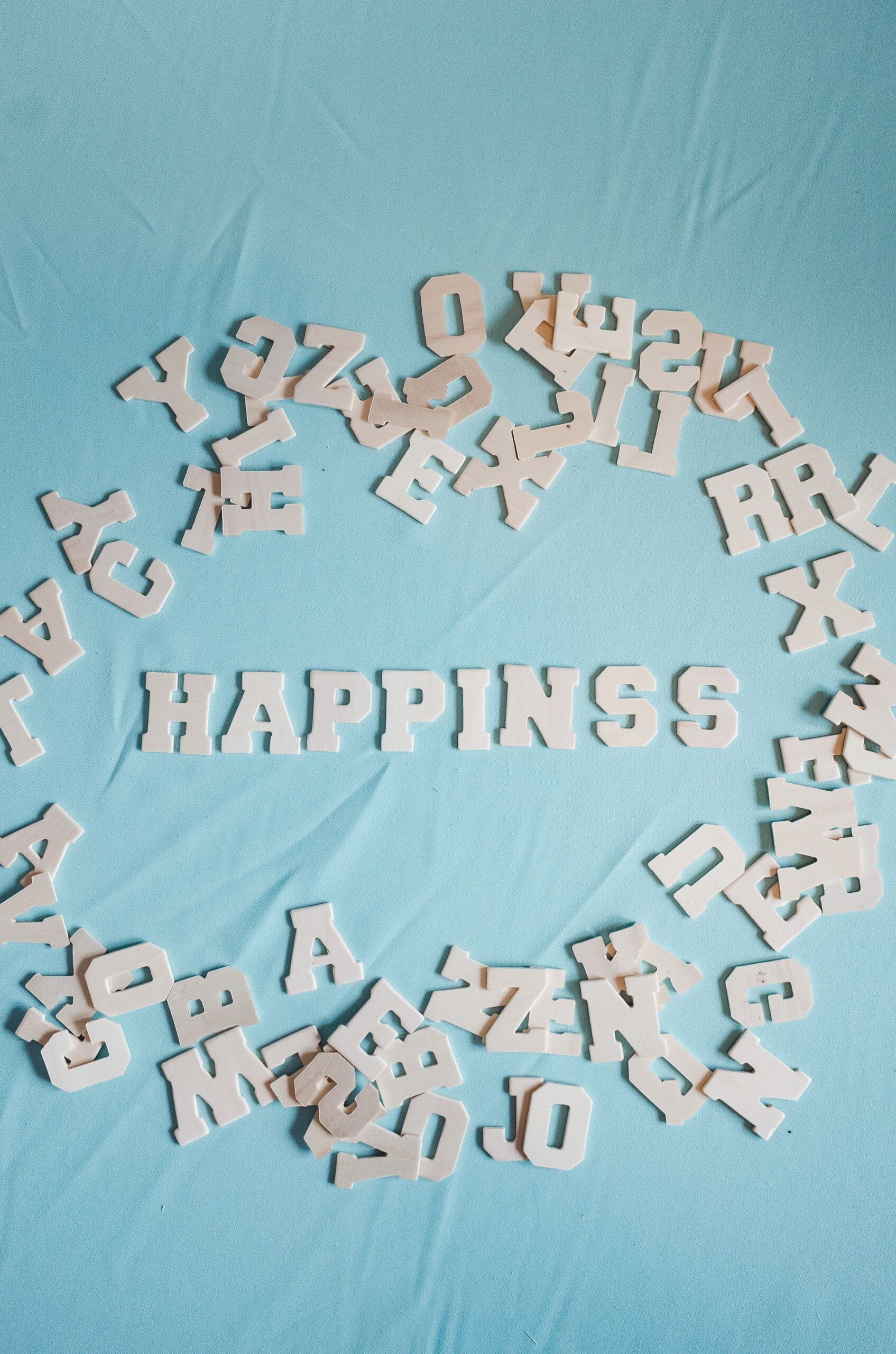 White wooden letters on a blue background spelling 'Happiness'.