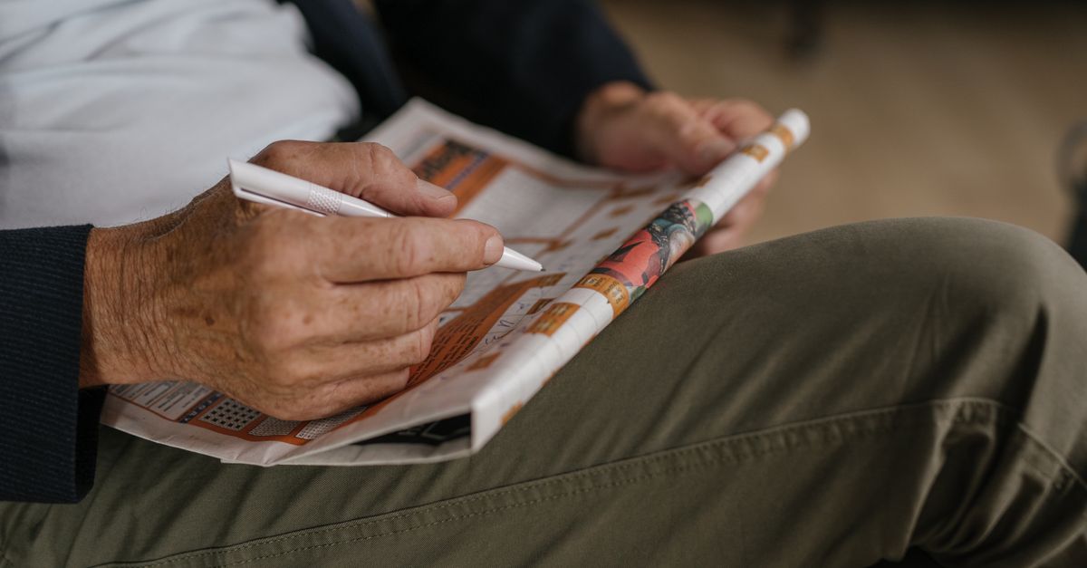 Senior man solving a crossword puzzle in a newspaper with a pen