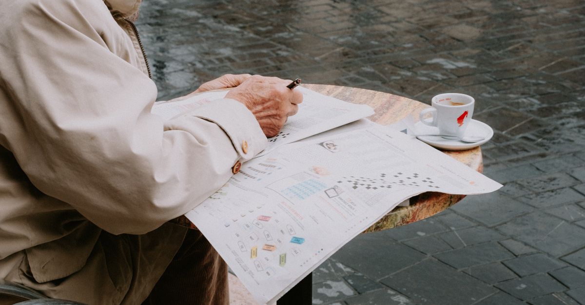 Senior man solving a newspaper crossword at an outdoor cafe table