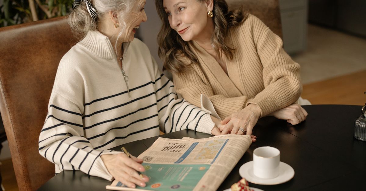 Two women sharing coffee while solving a crossword puzzle together