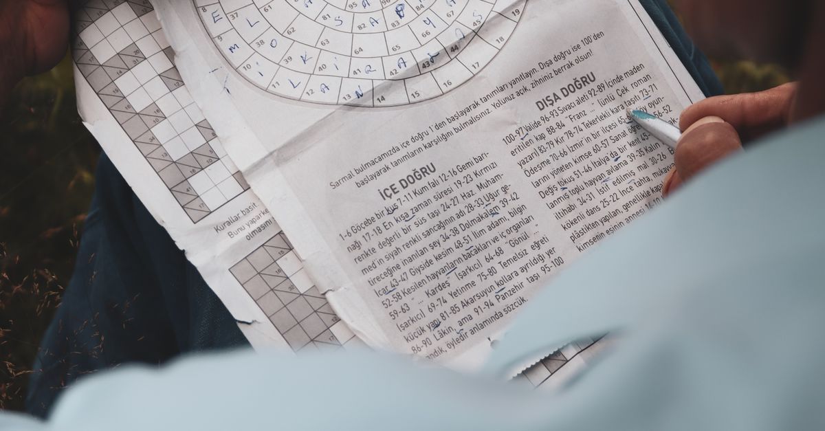 Elderly person solving a crossword puzzle outdoors in a calm setting