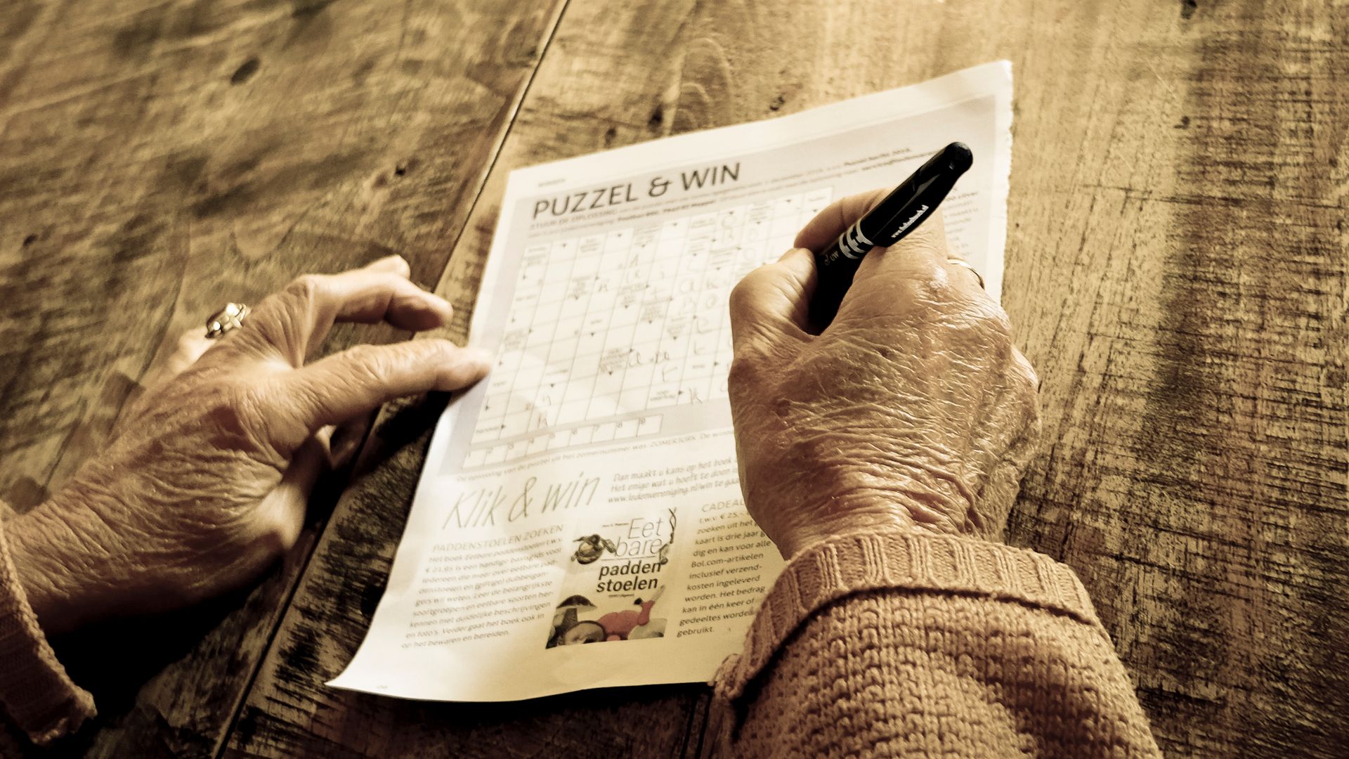 Senior adult solving a word puzzle with a pen on a wooden table