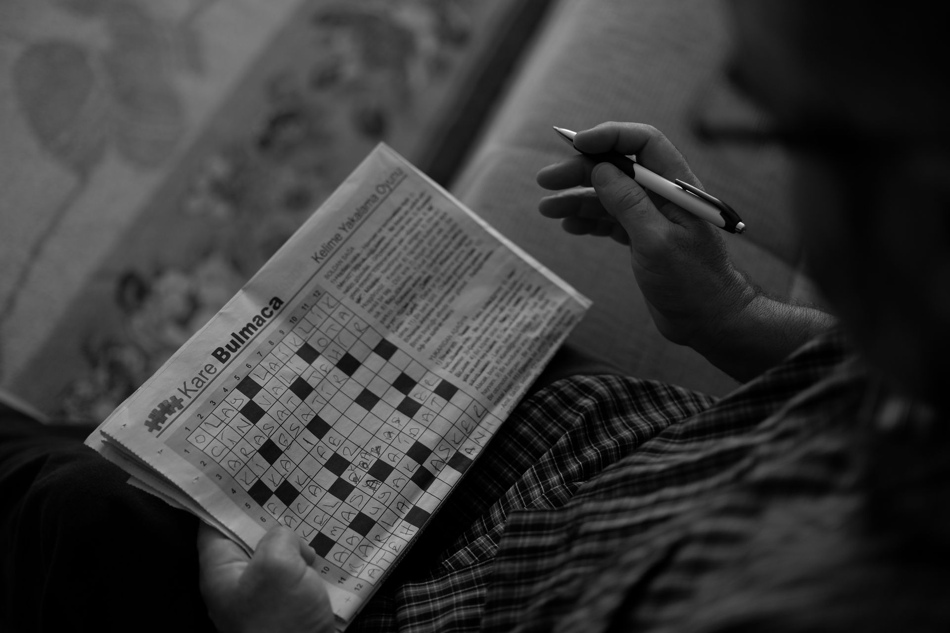 Person solving a crossword puzzle indoors with a pen