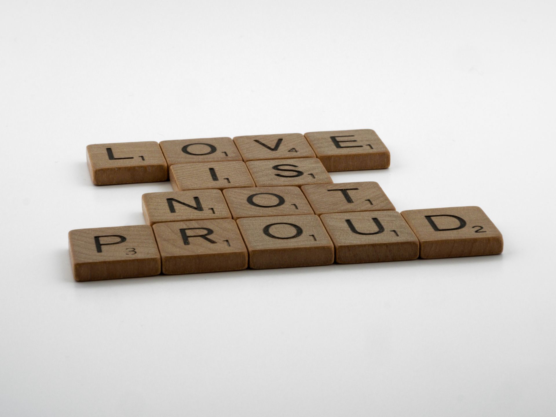 Wooden tiles spelling Love is not proud on white