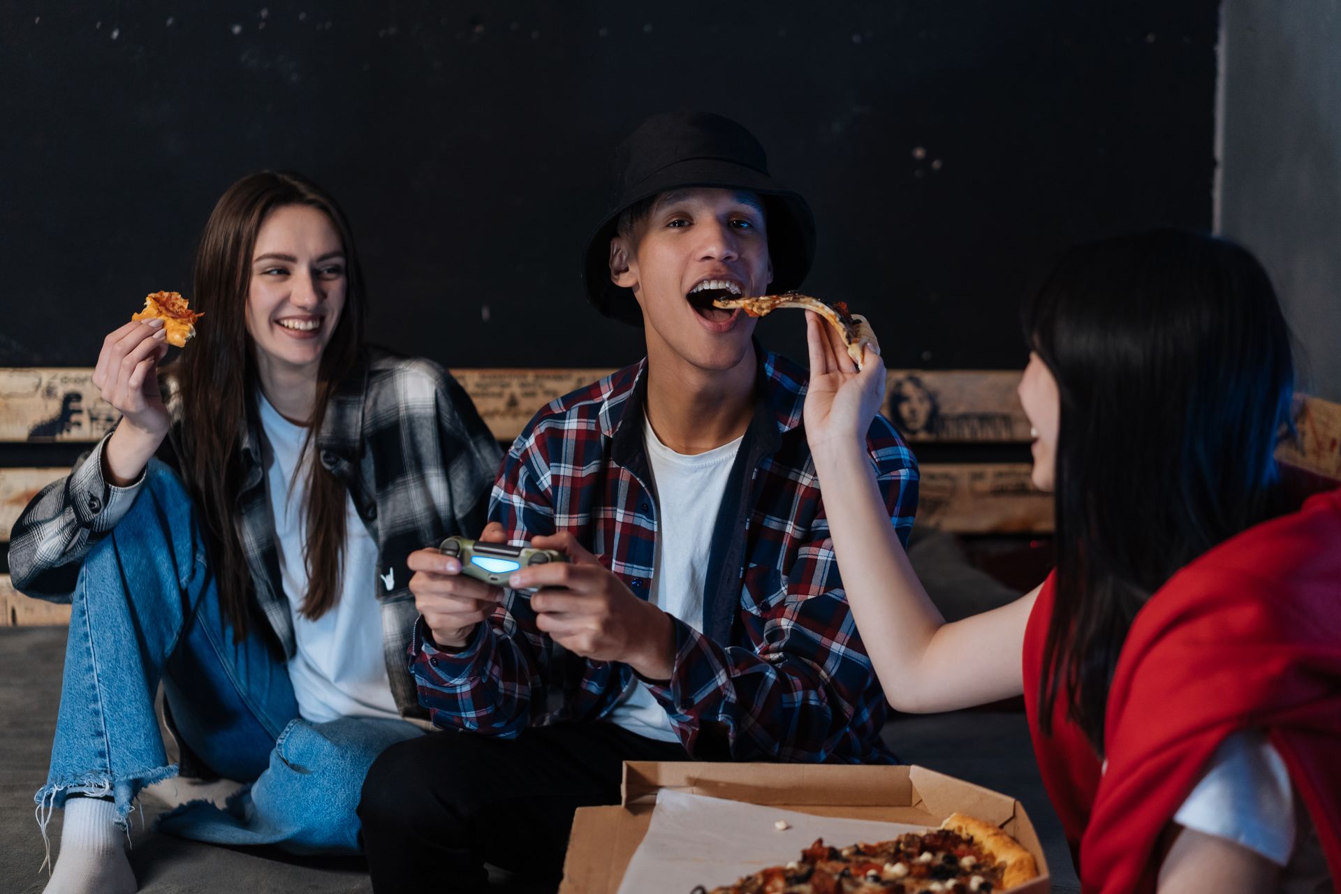 Three friends sharing pizza and playing games together