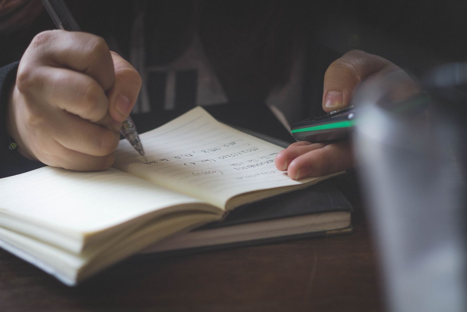 Person writing notes while using a phone