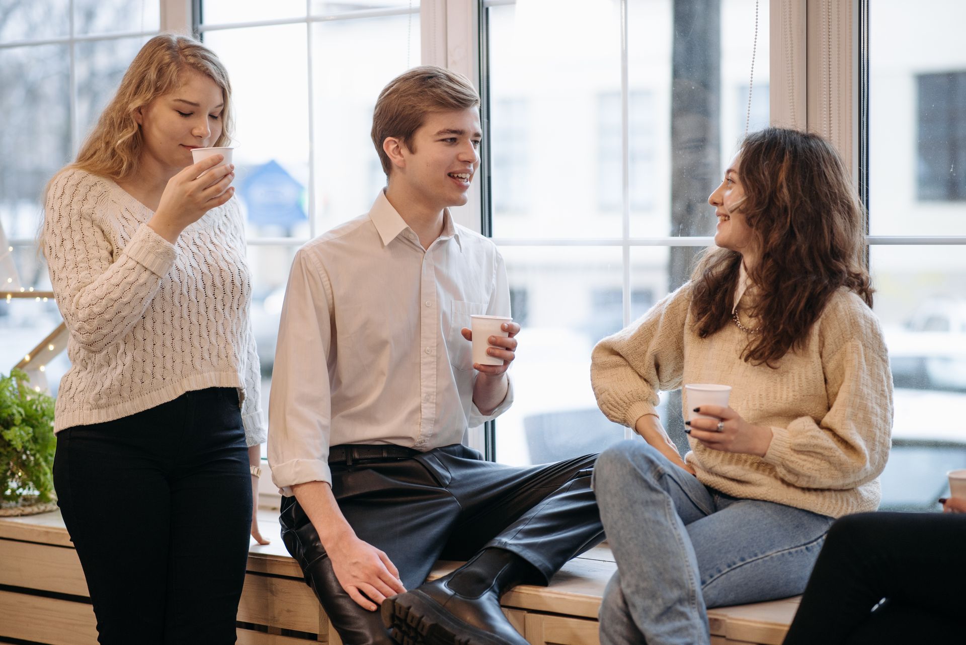 Three young adults enjoying coffee and conversation by a window