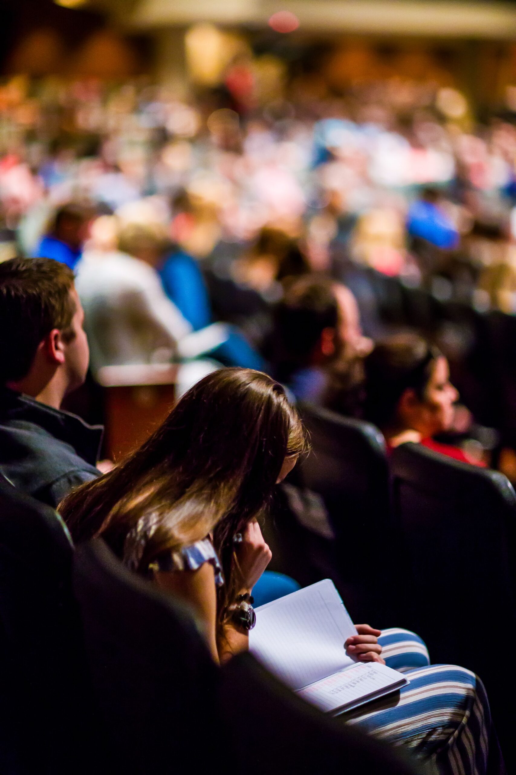 Person reading amidst a large audience in a university auditorium