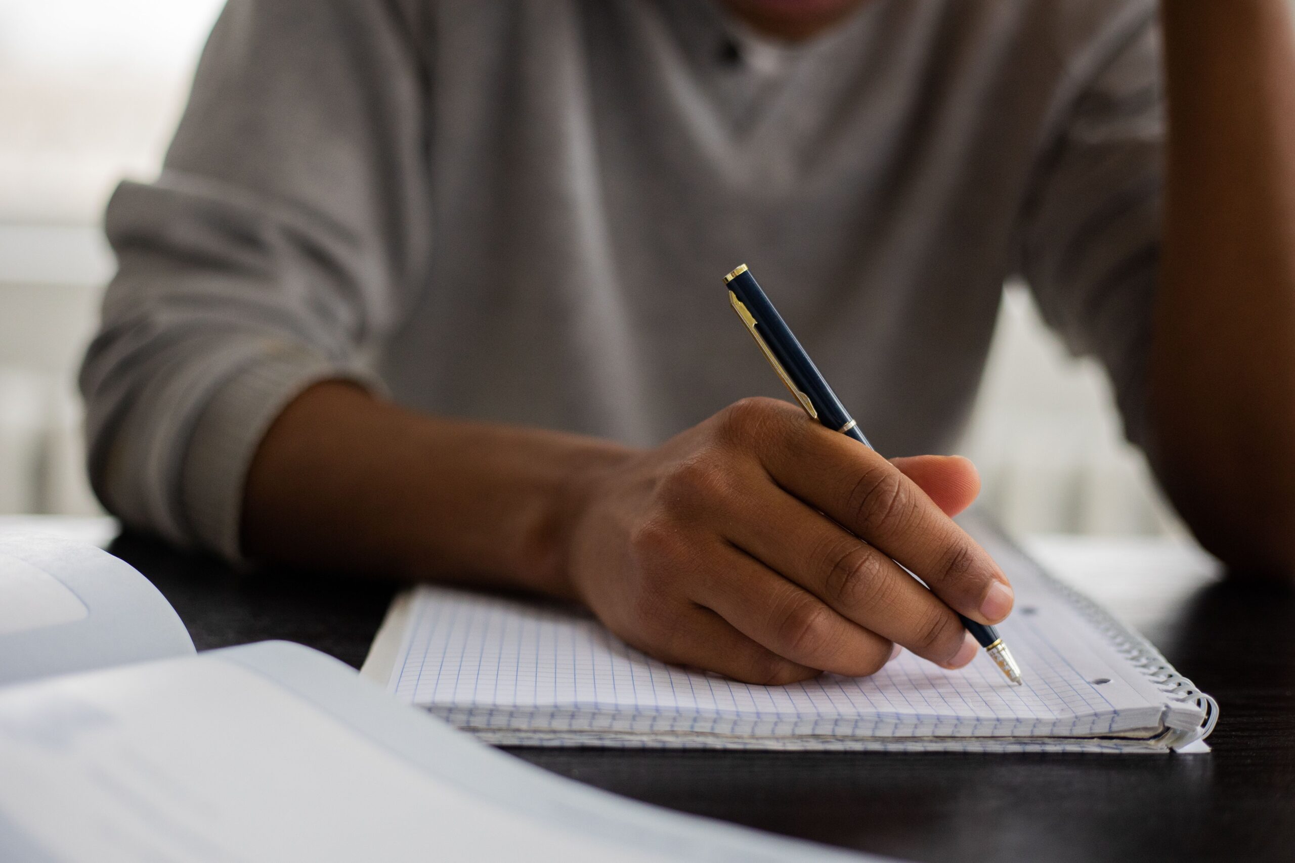 Close-up of a student writing notes in a notebook with a pen, emphasizing academic focus.