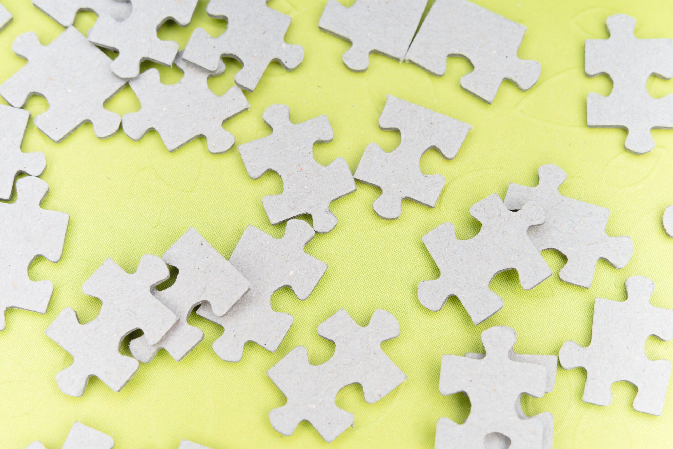 Close-up of gray puzzle pieces scattered on a vibrant yellow background for a playful abstract composition.