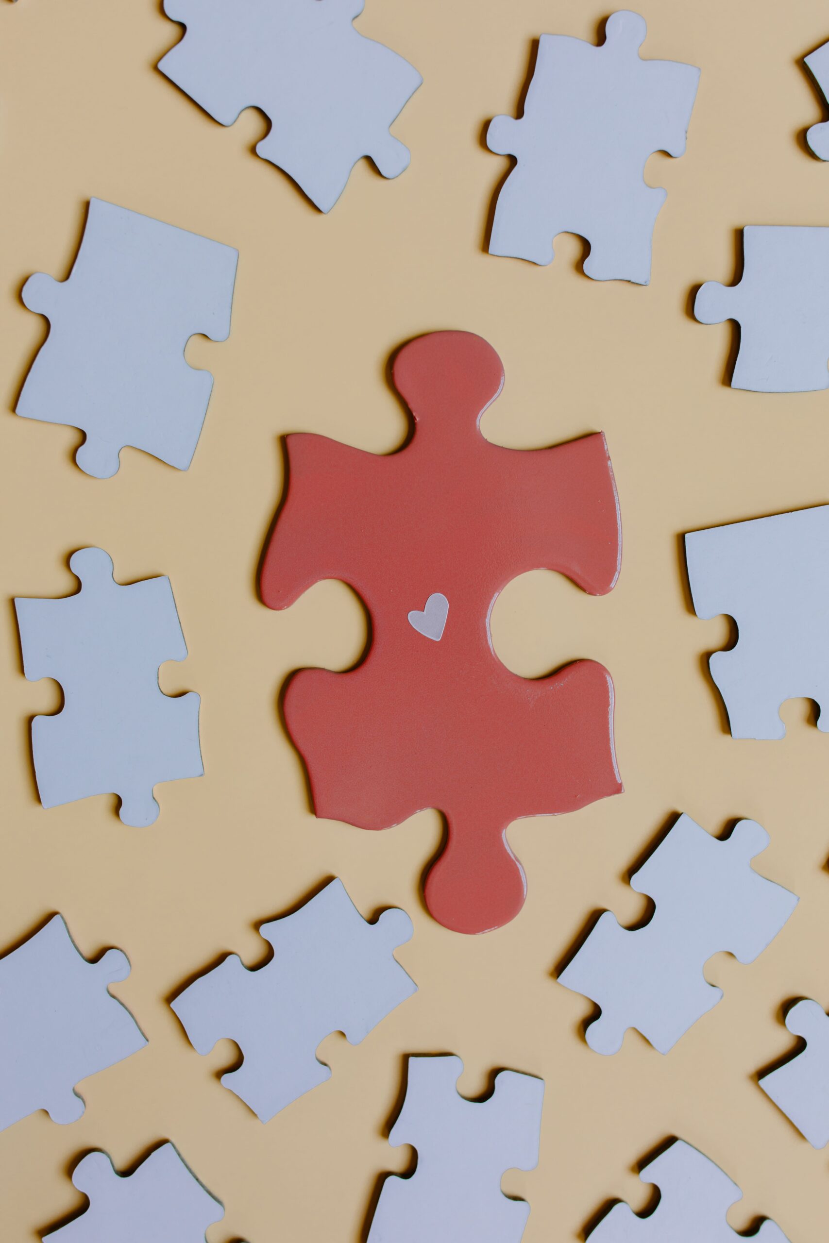 A red puzzle piece with a heart on a yellow surface surrounded by white puzzle pieces.